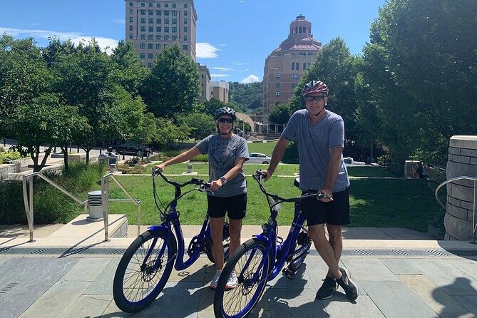 A couple poses with their bikes with downtown Asheville in the background
