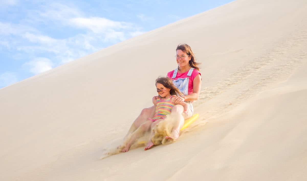 family sledding down a sand dune