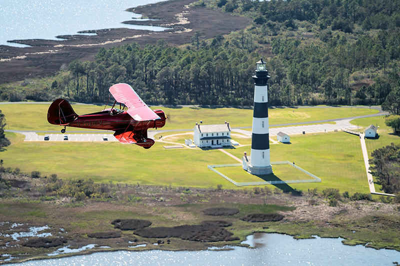 red biplane flying past a lighthouse on the outer banks of NC