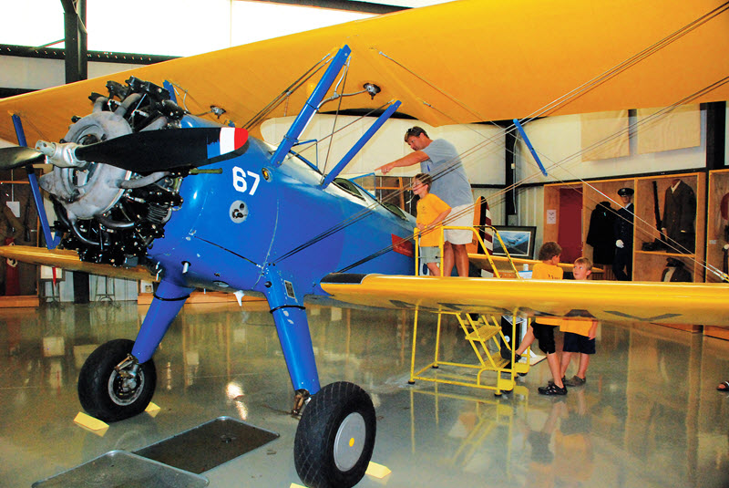 A father and son explore a blue and yellow biplane at the North Carolina Aviation Museum in Asheboro, NC