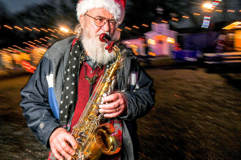 Older man with a Santa hat playing the saxophone outside.