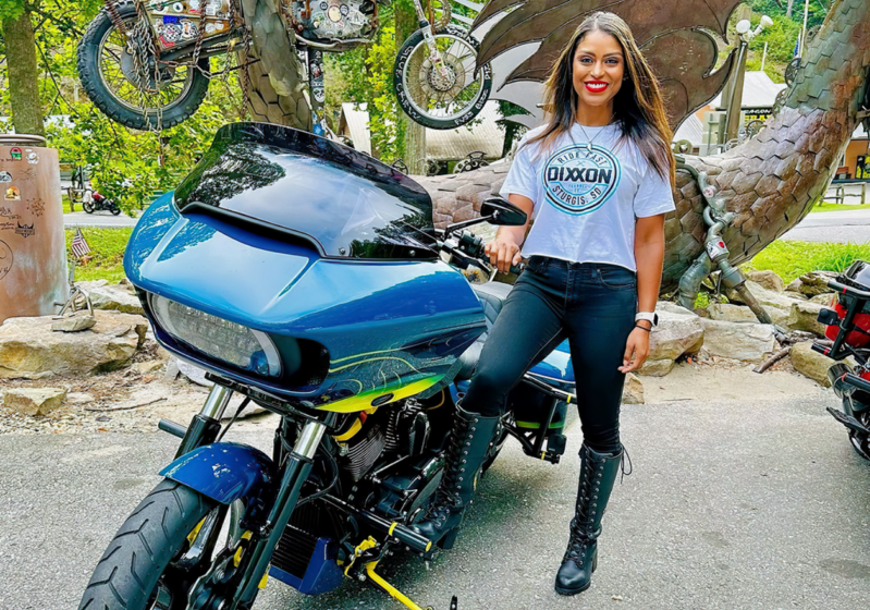 Woman standing in front of Tail of the Dragon at Deals Gap with her motorcycle