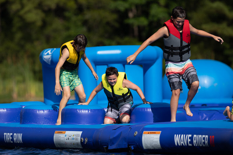 Three boys bounce across a water obstacle course at the Charleston Aqua Park