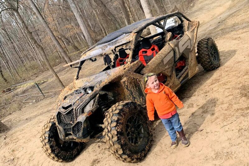 Kid standing in front of a muddy ATV at Carolina Adventure World