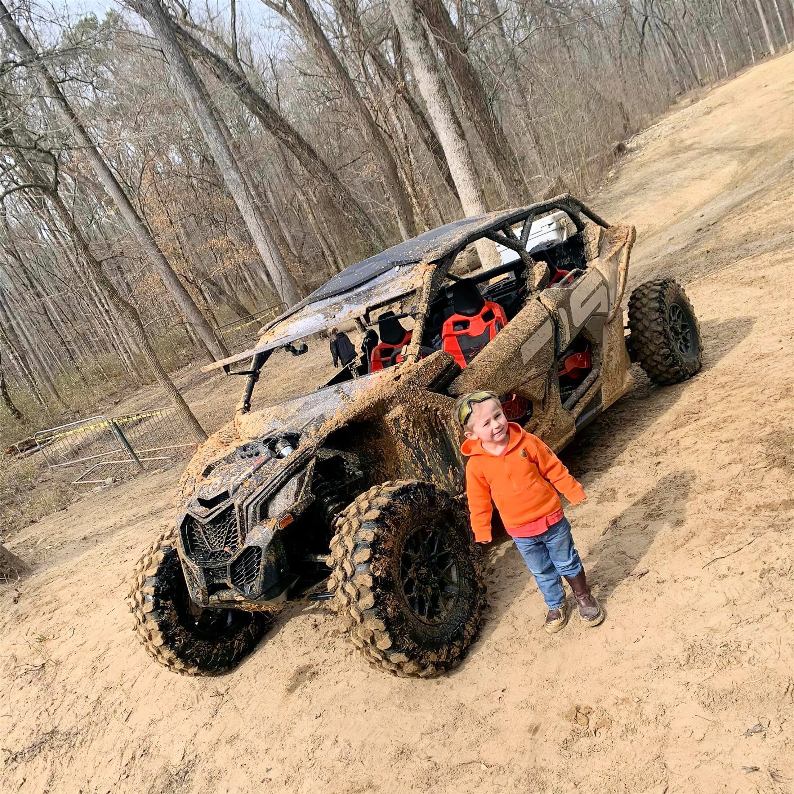 Kid standing in front of a muddy ATV at Carolina Adventure World