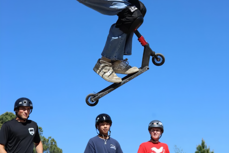 Guys watching someone do a stunt on a scooter at Daniel Dhers Action Sports Complex