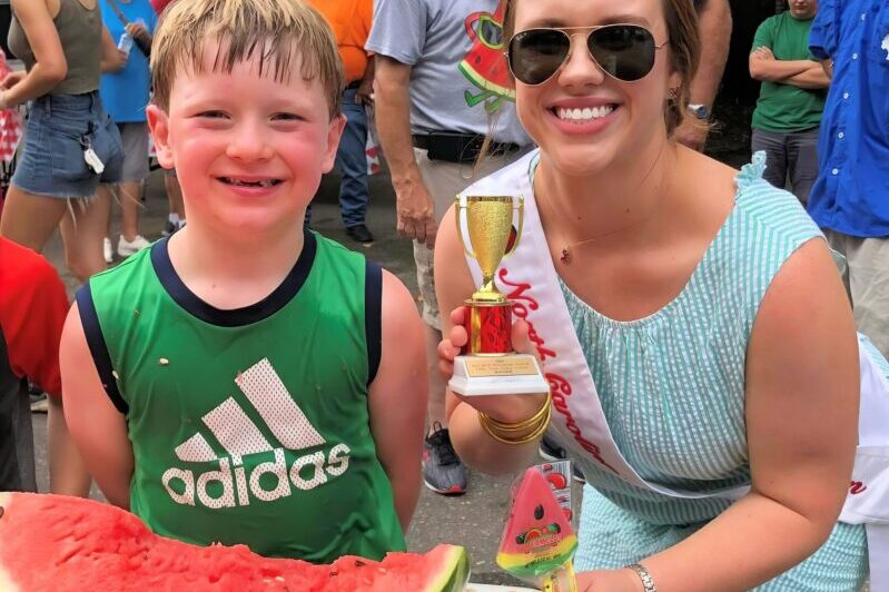 Kid standing in front of a half-consumed watermelon receiving a trophy