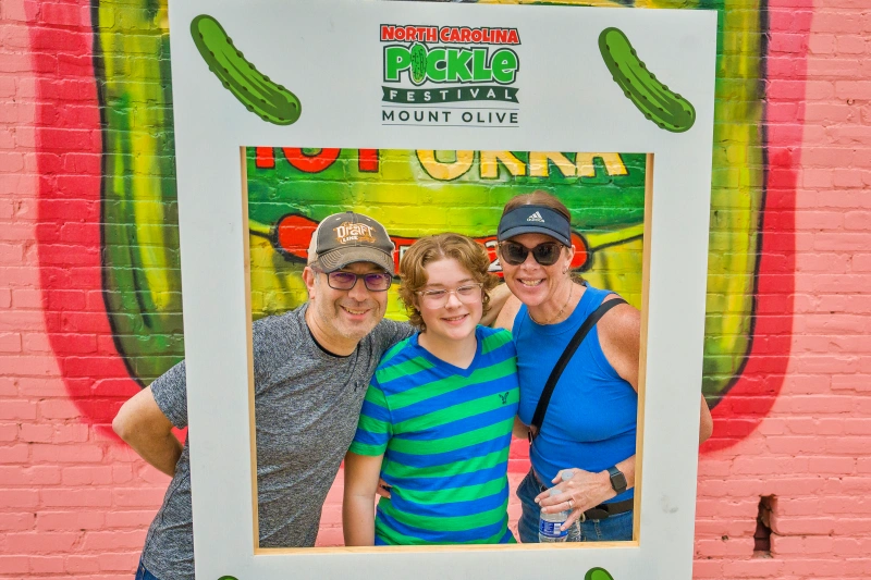 A father, son, and mother pose in a frame at the NC Pickle Festival